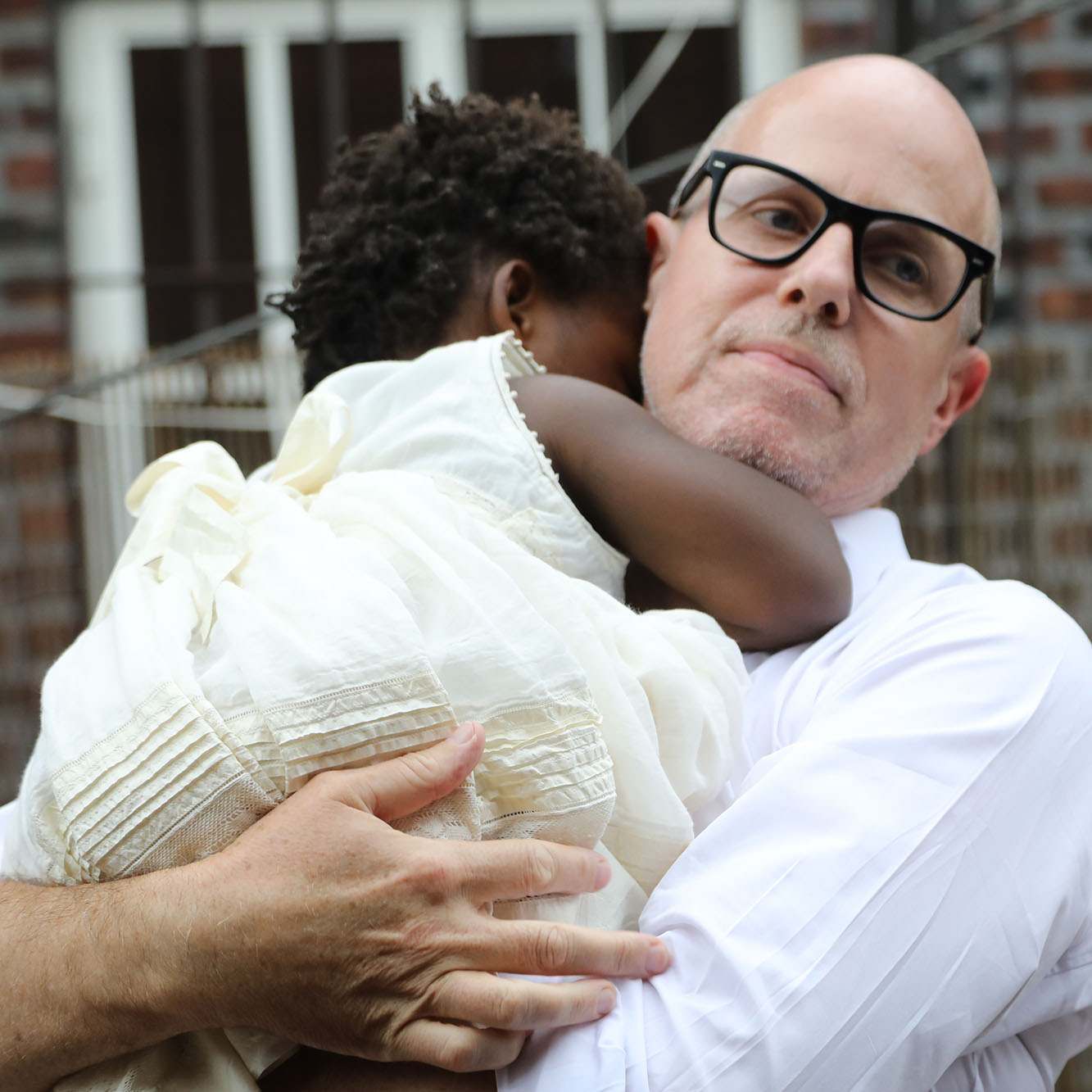 an with black glasses and white shirt holding a little girl in white dress.