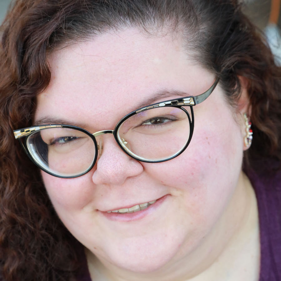 Woman with brown curly hair and cat eye shaped glasses looking into the lens.