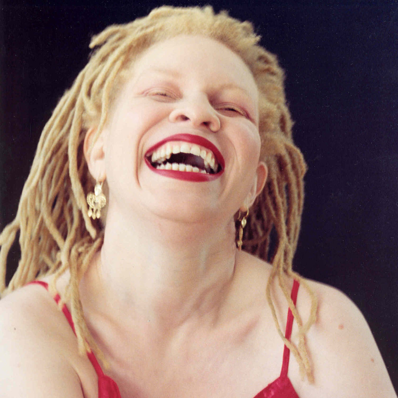 Woman with blond dreads and bright red lips laughing.
