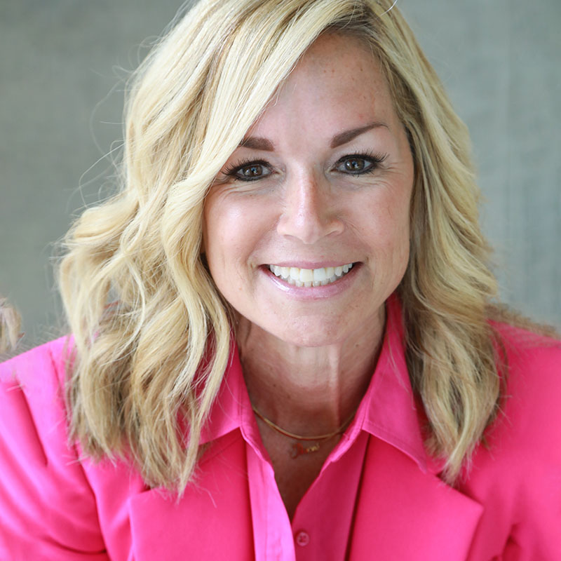 Light-skinned woman with blond hair and bright pink suit jacket, smiling.