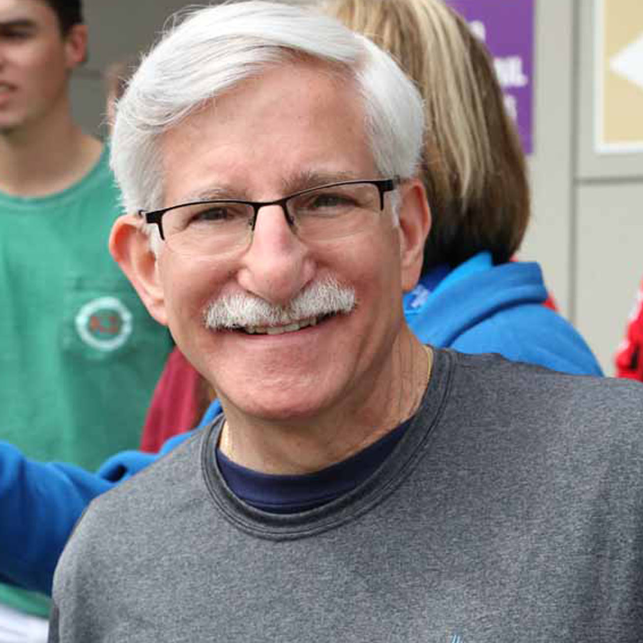 Man with white hair and mustache glasses and gray t-shirt.