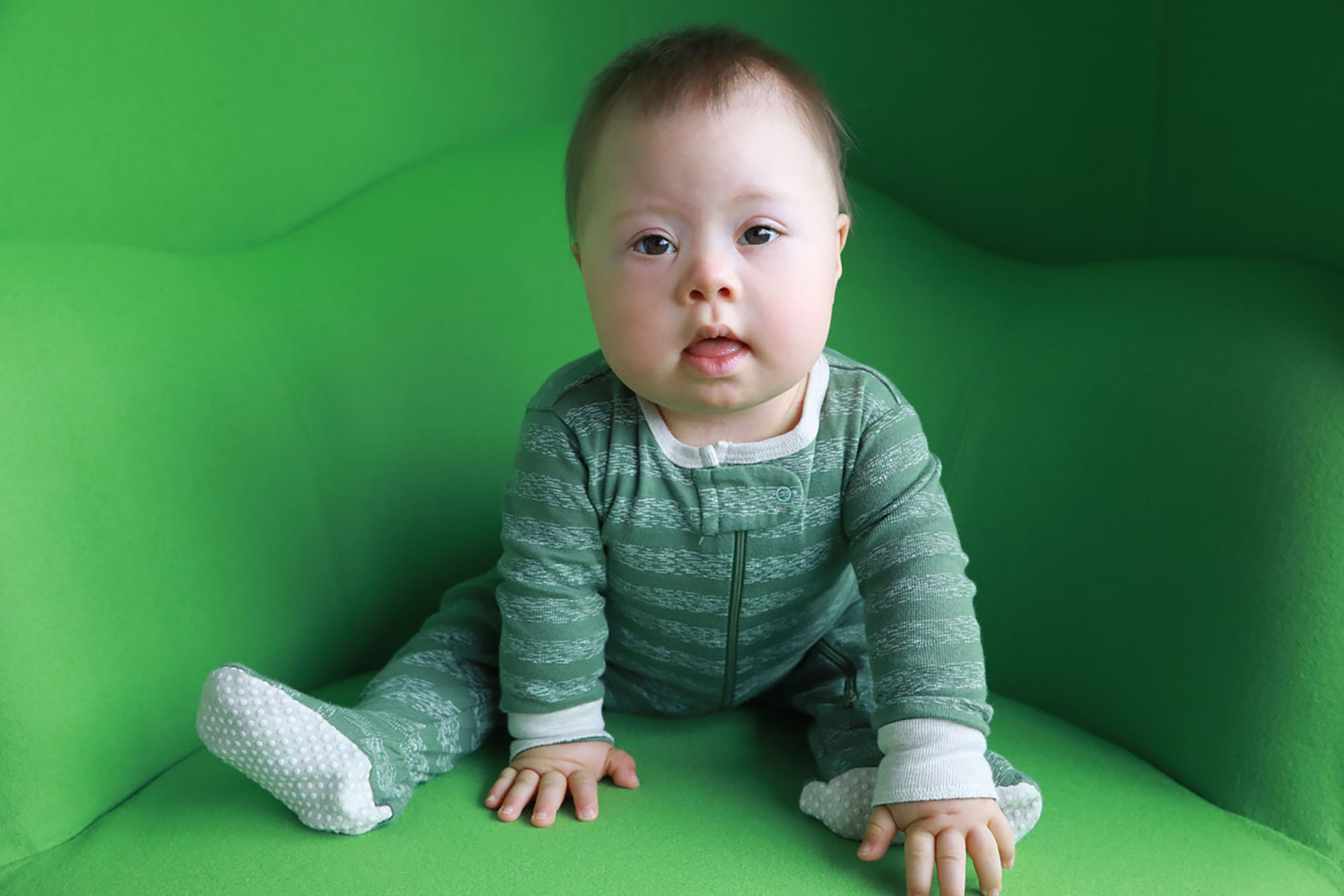 Baby in green striped onesy sitting on a green chair.