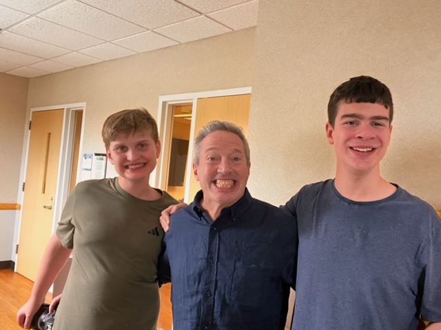 Rick standing between two tall young men one with brown hair the other with blond hair. Rick's hair is grey.