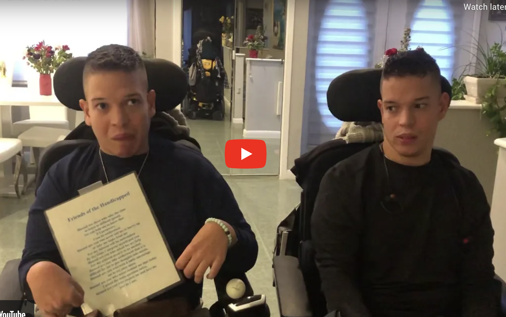 2 guys in wheelchairs. 1 is holding a printed poem.