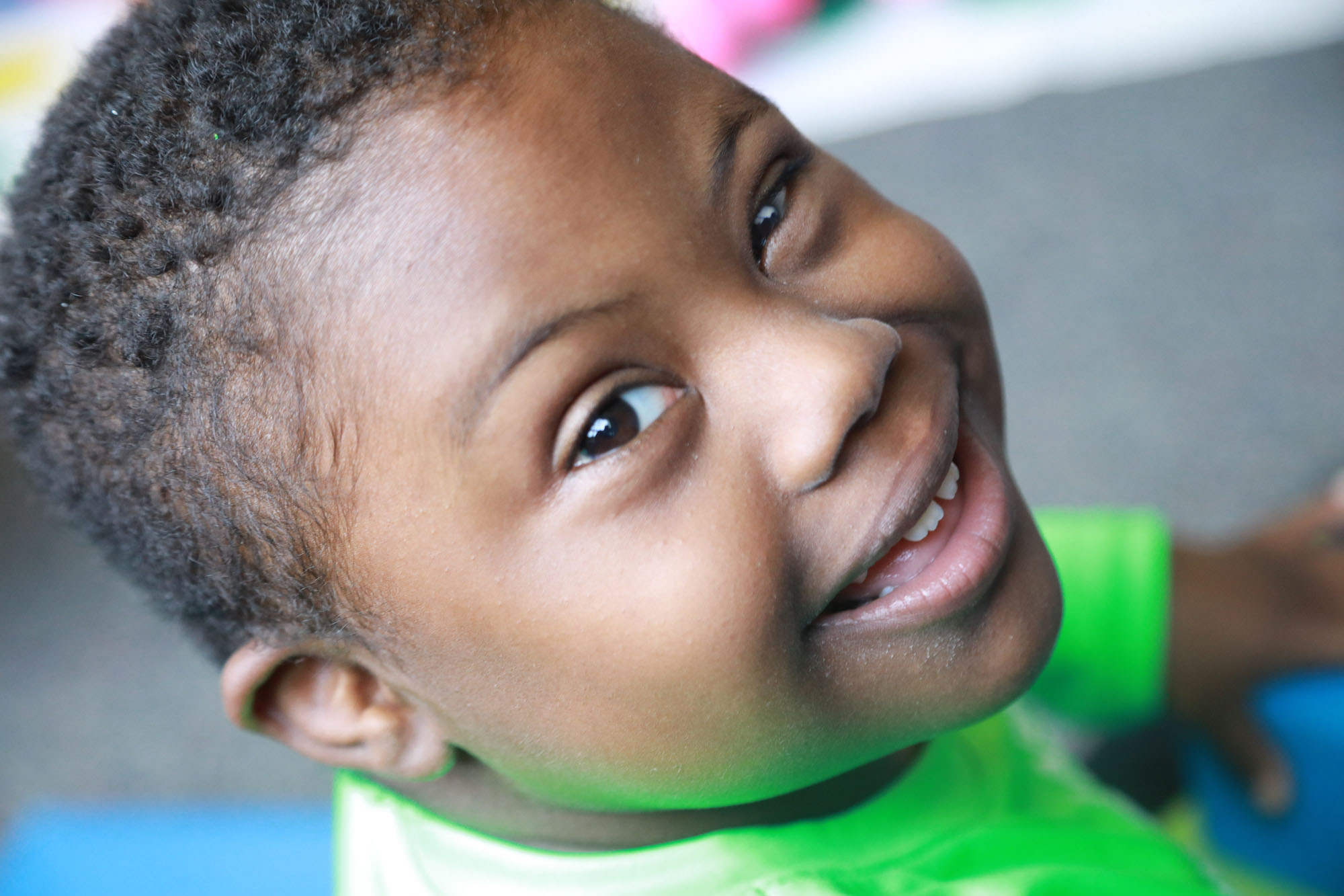 Young boy in green shirt smiling into the camera.
