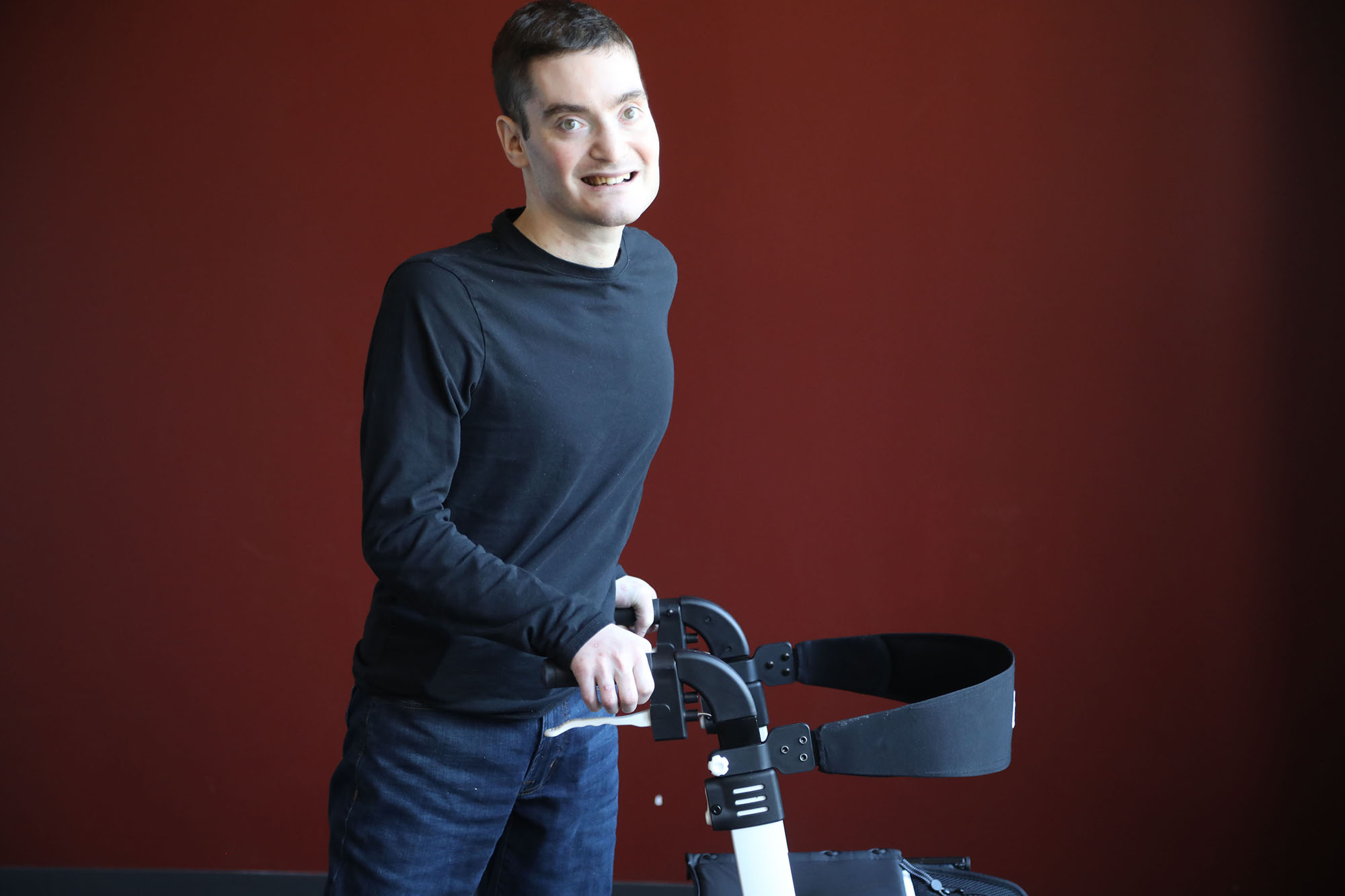 Man with Familial Dysautonomia stands in front of dark red background