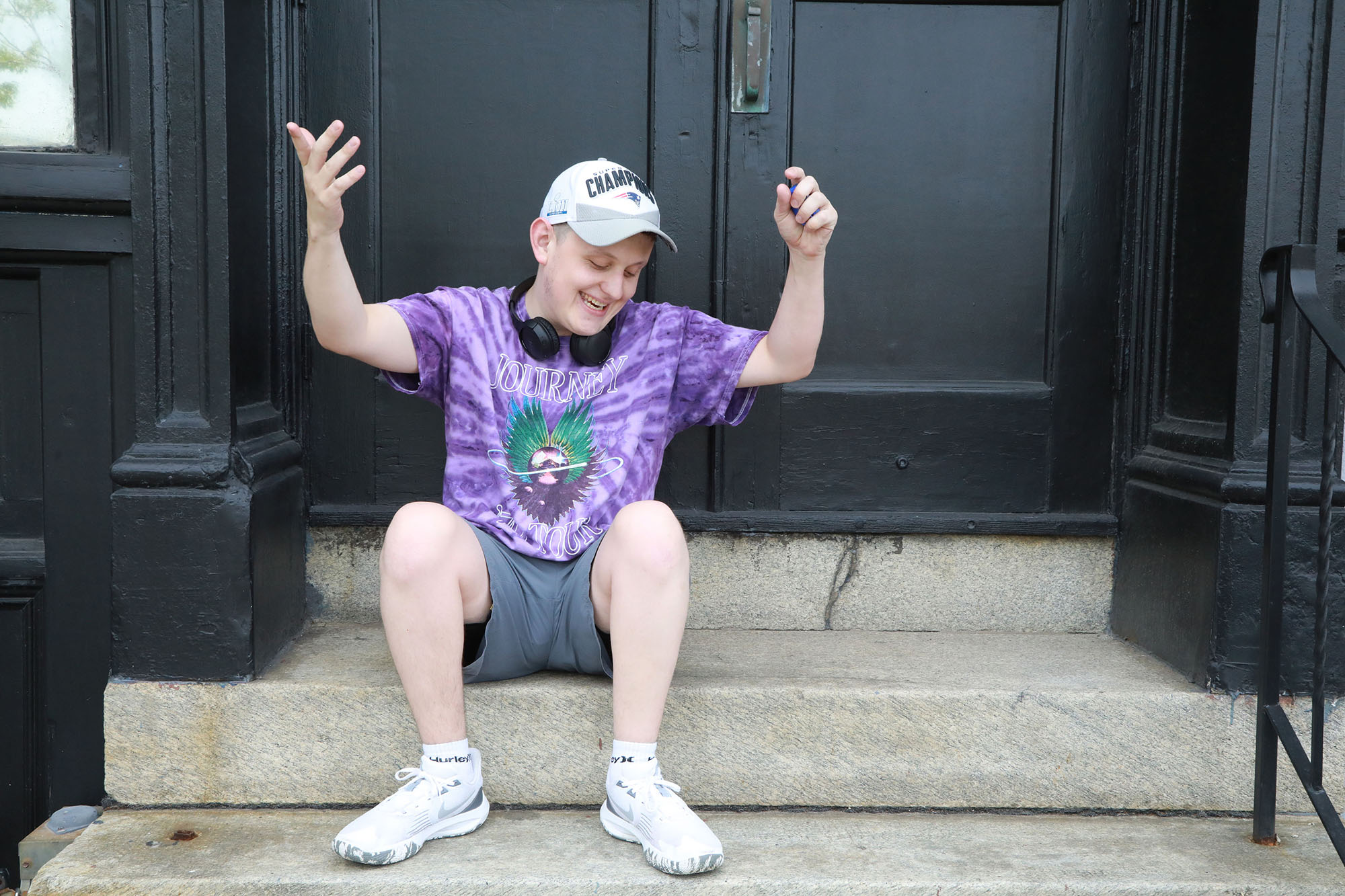 Man with autism wearing purple shirt sits on steps with arms up.