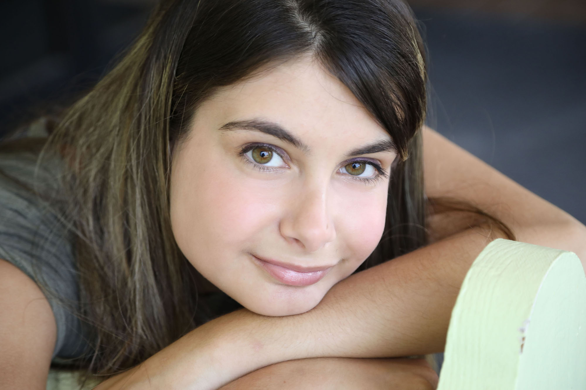young woman with Autism resting chin on her arms looks into camera.