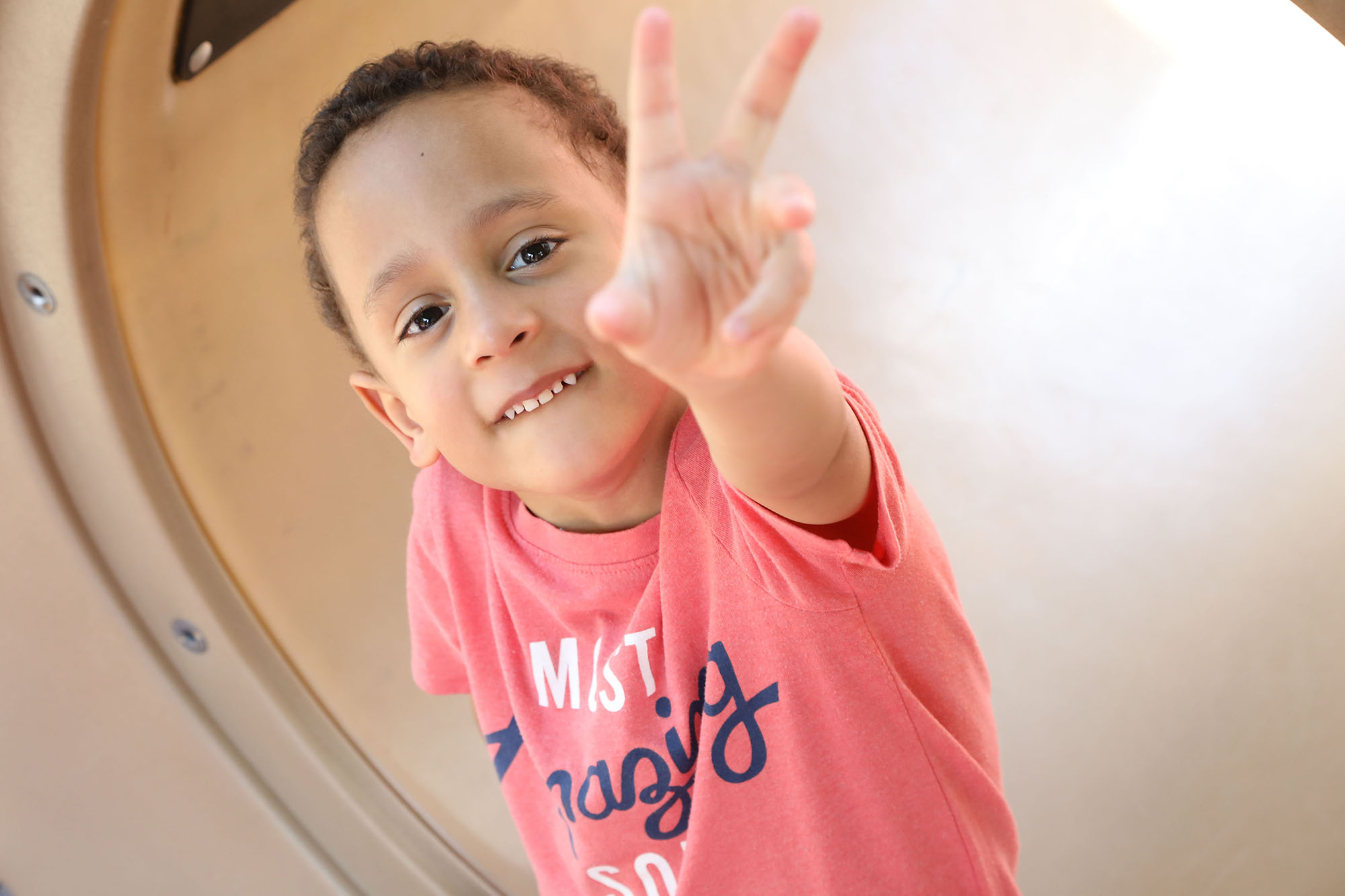 young boy with autism wearing red shirt holds peace sign up to camera