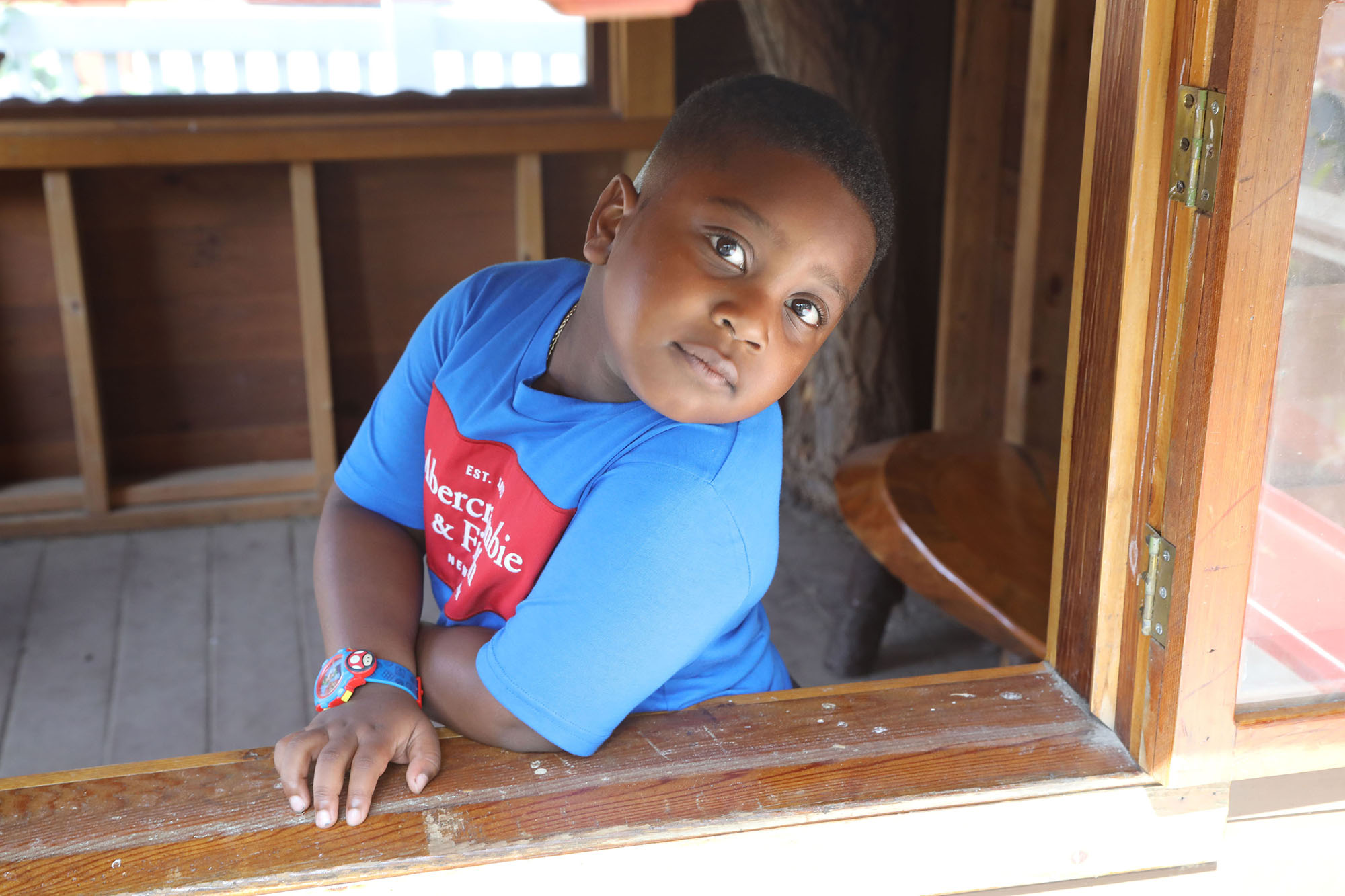 young boy with Autism wearing a blue shirt and looking through window frame