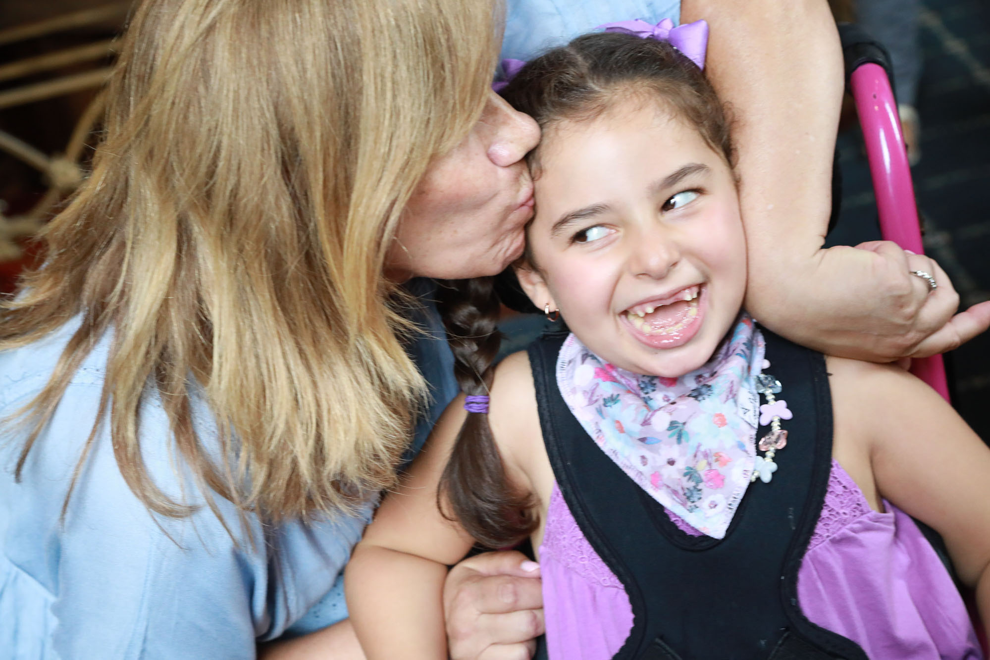 young girl wearing purple shirt gets kissed by her mother