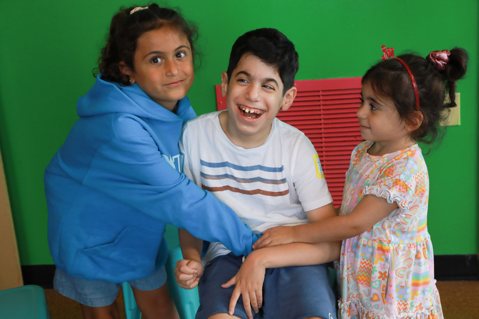 boy wearing white shirt and sitting down poses with his two sisters