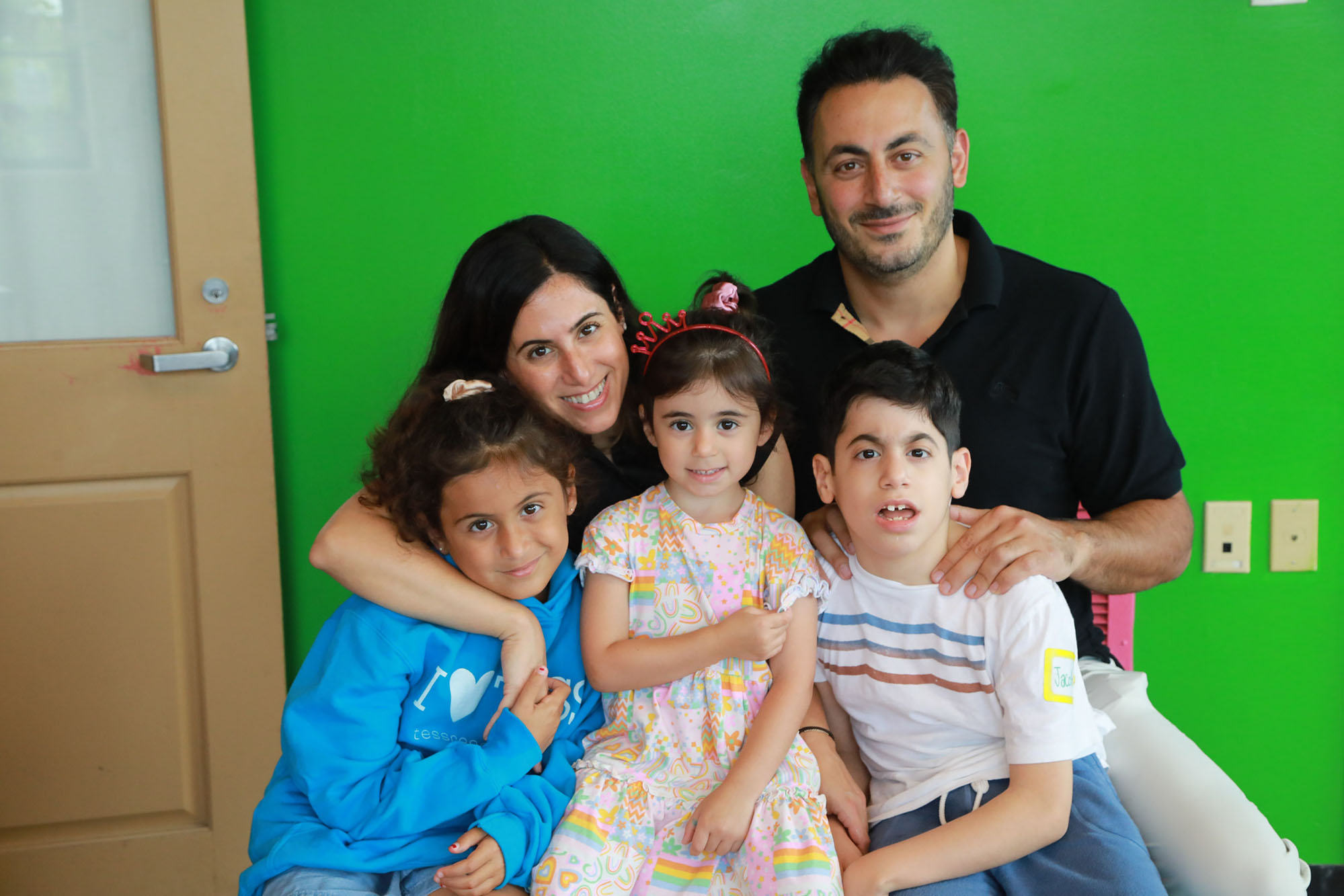 young boy wearing white shirt poses with his two sisters and mother and father