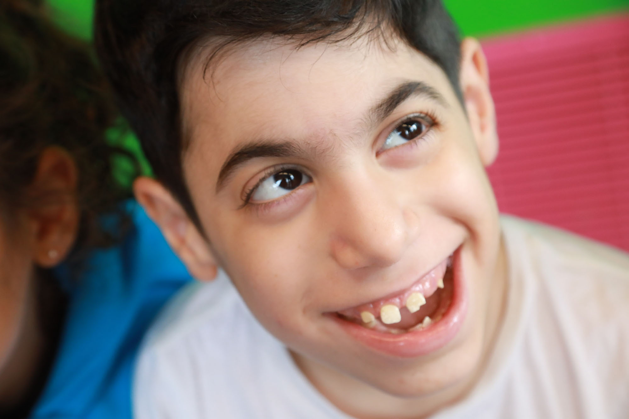 young boy wearing white shirt smiles while looking to the right, closeup photo