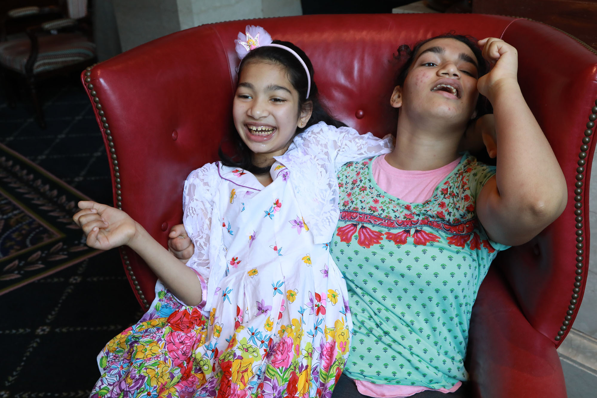 girl wearing green and red shirt sitting on a red chair with her sister