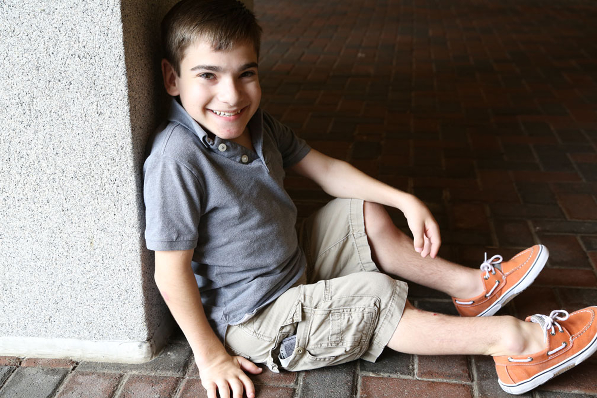 boy with skeletal dysplasia sitting down against a wall