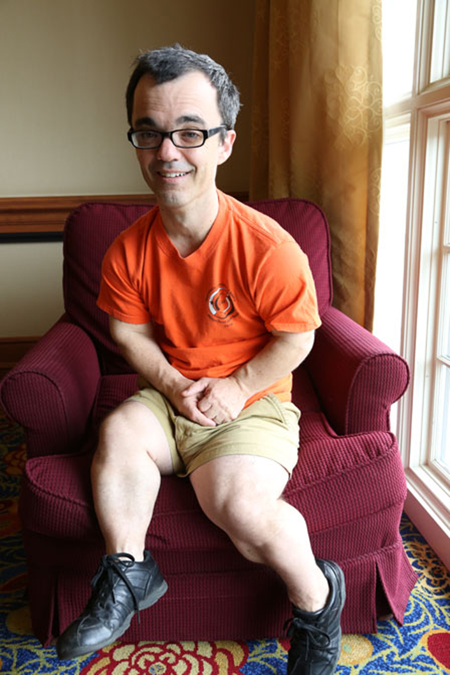 man with skeletal dysplasia wearing orange shirt sitting down