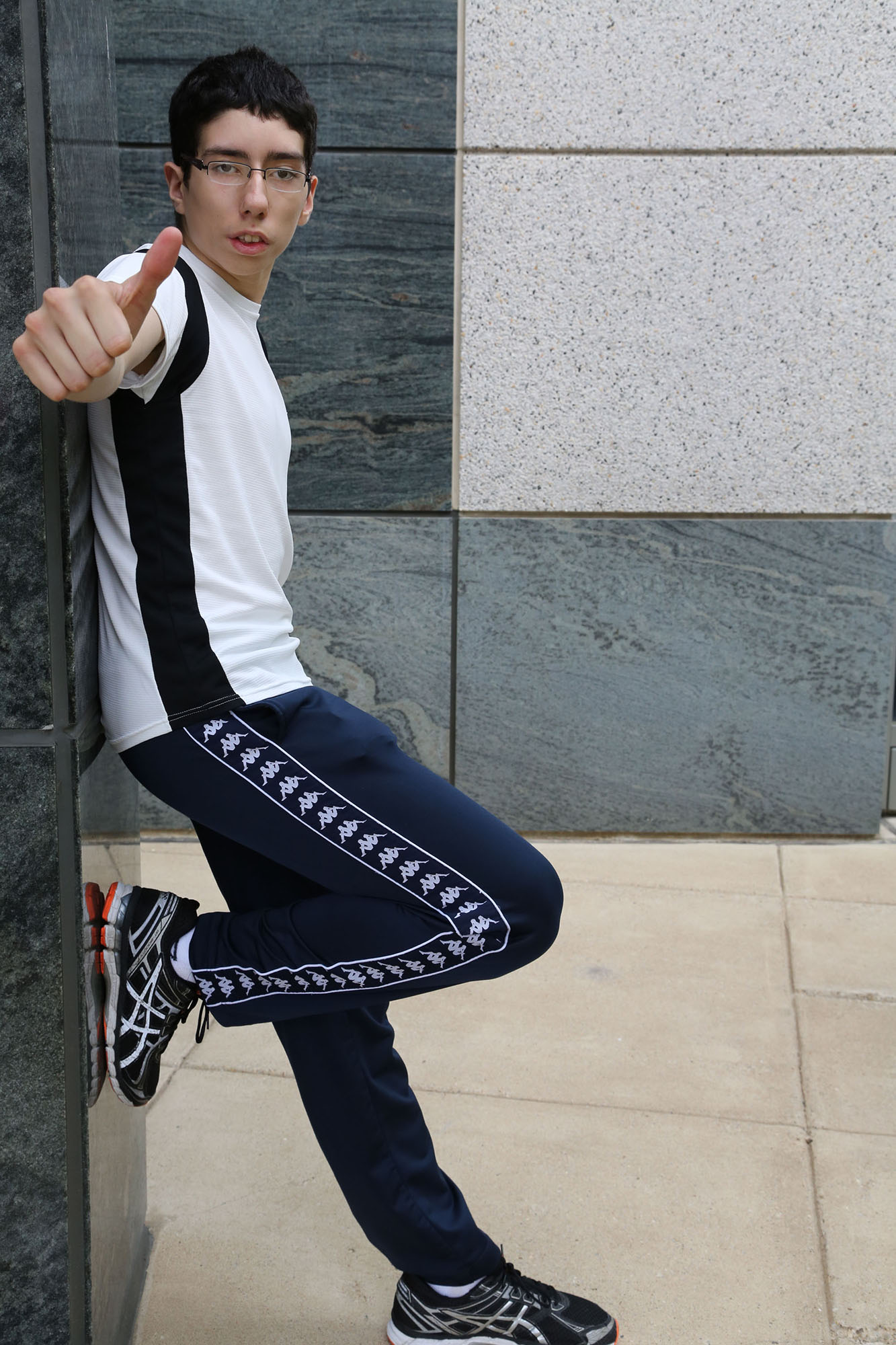 boy with moebius syndrome leaning against walls gives a thumbs up