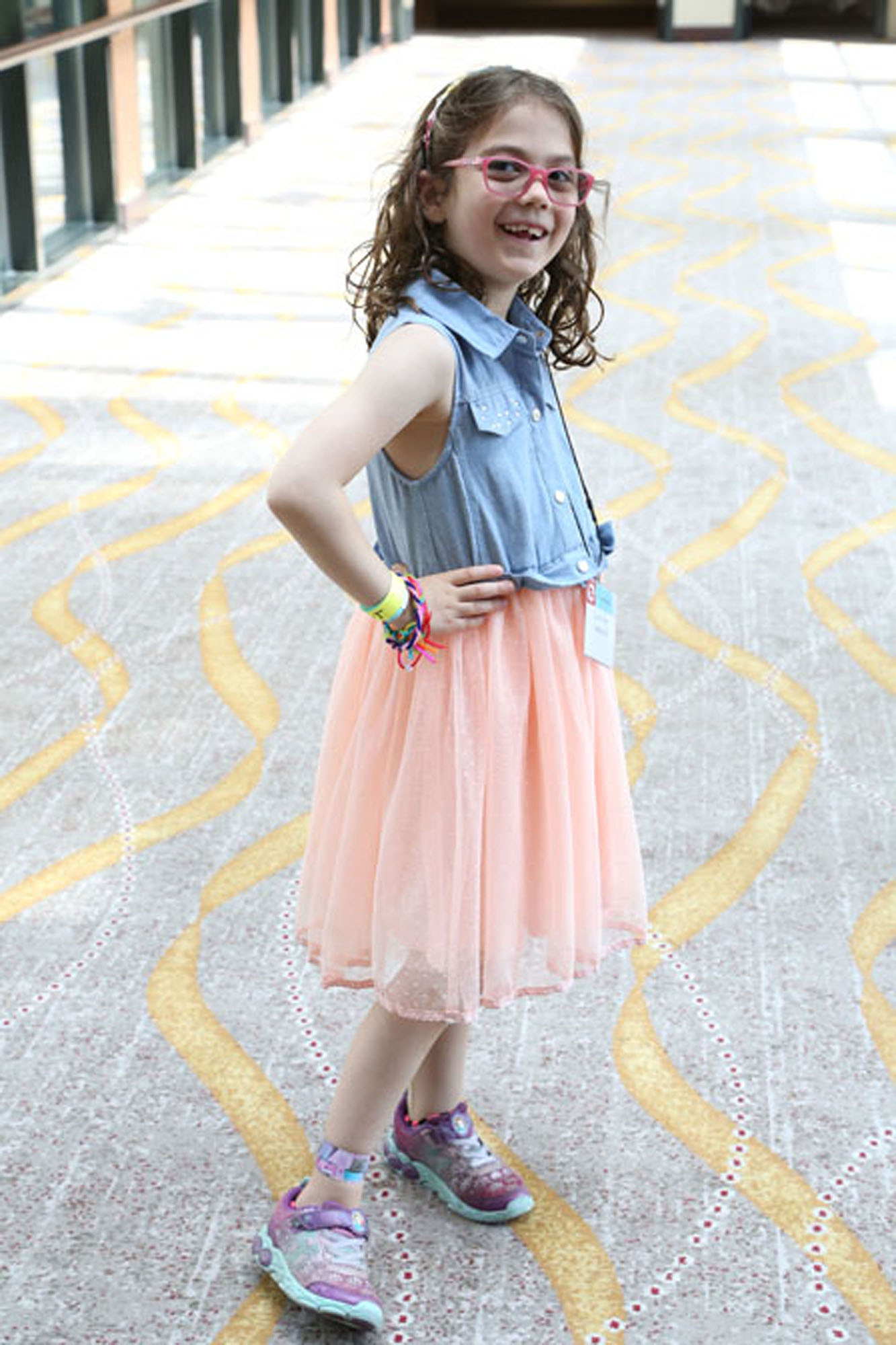 young girl with klippel trenaunay syndrome wearing blue and pink outfit looks at camera