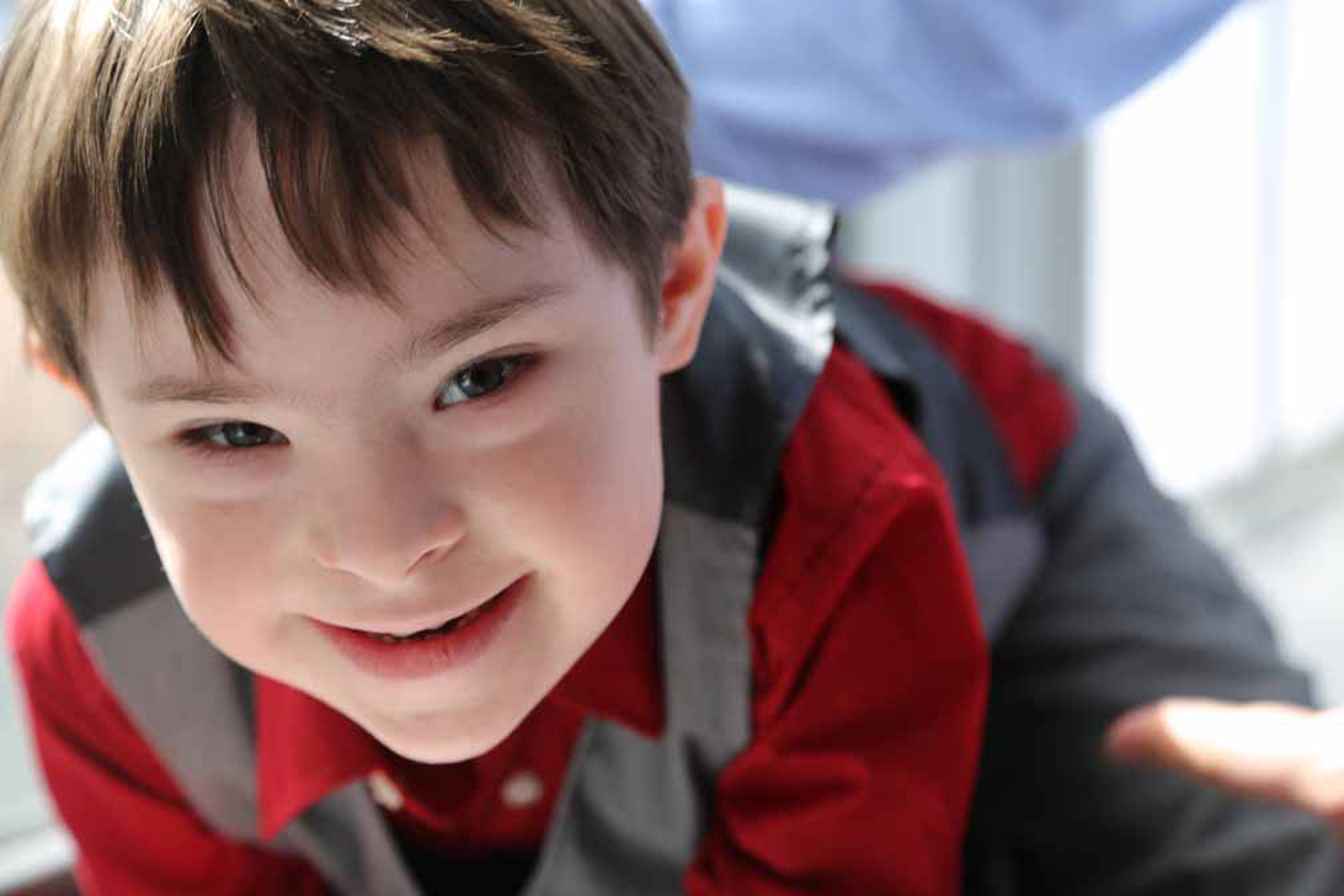 young boy with down syndrome wearing red and grey outfit smiling at the camera