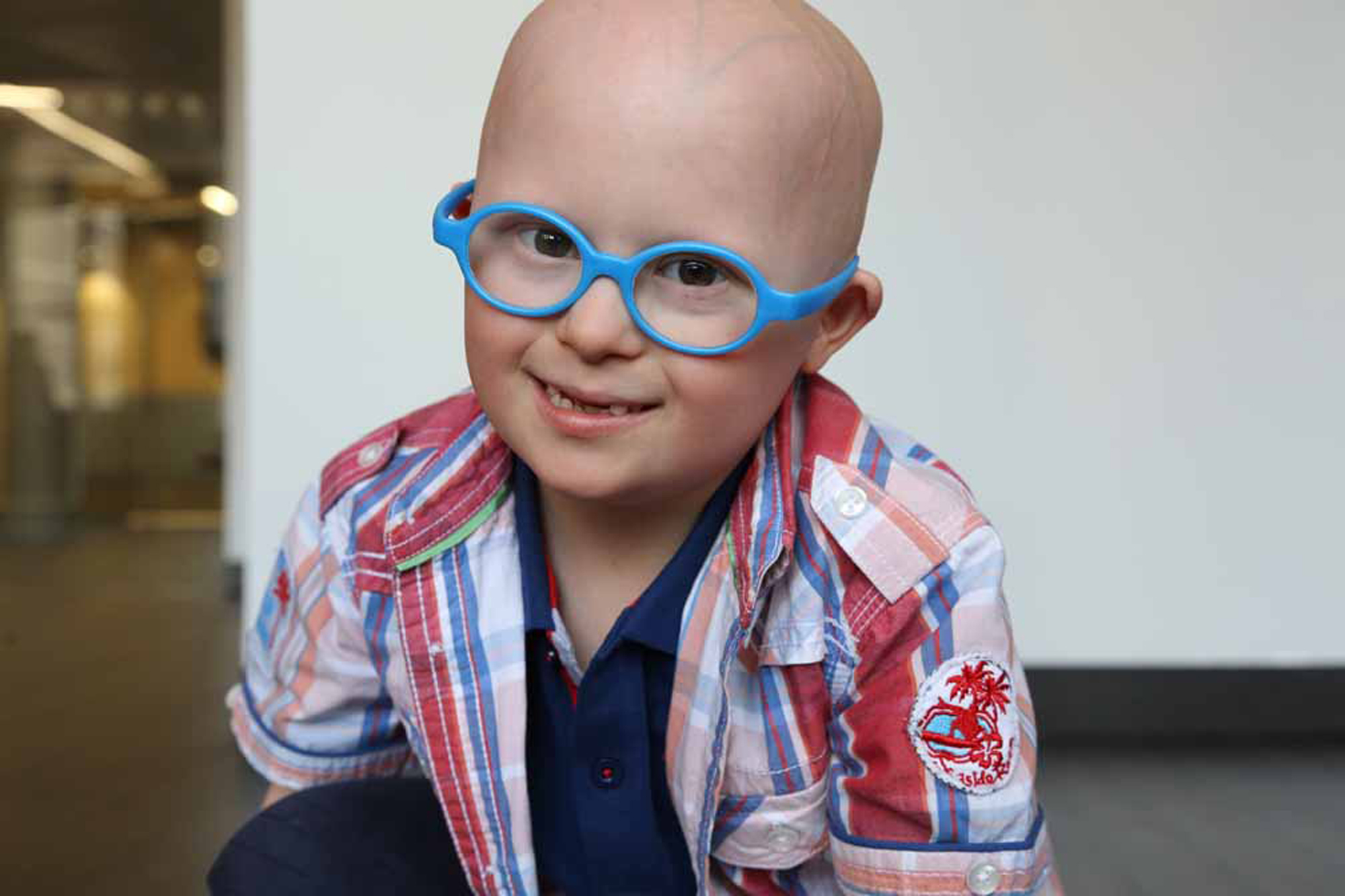 Young kid with down syndrome wearing blue glasses smiling at the camera