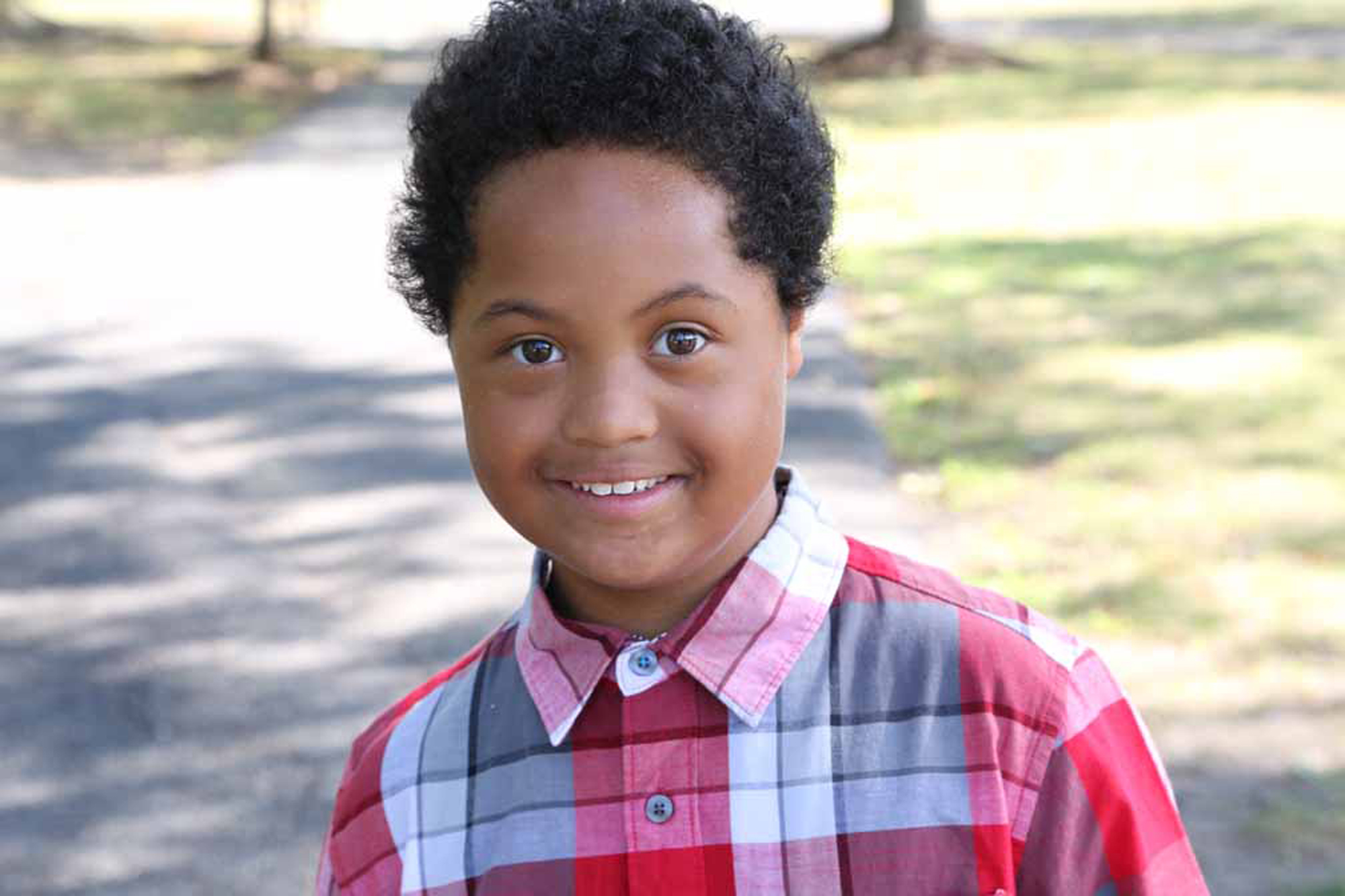 young boy with down syndrome wearing plaid shirt smiling at the camera