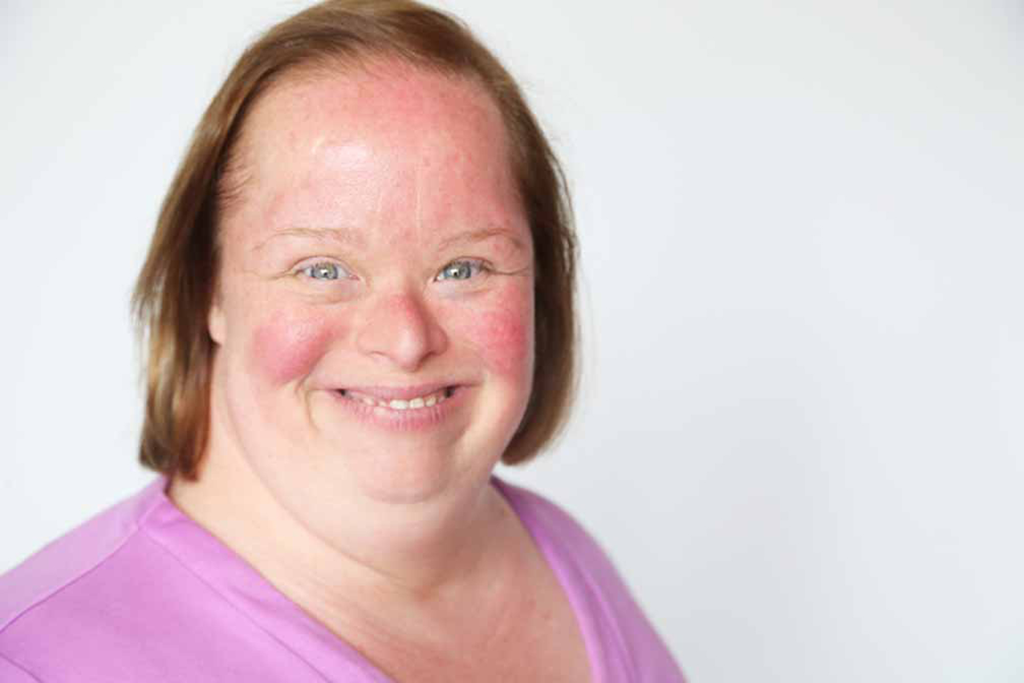 woman with down syndrome wearing pink shirt smiling at camera