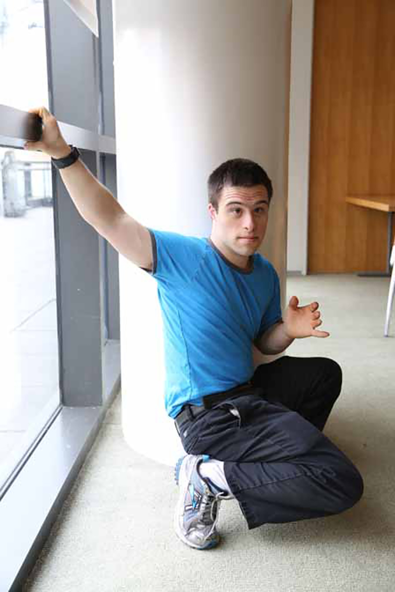 Man with down syndrome wearing blue shirt squatting looks at camera