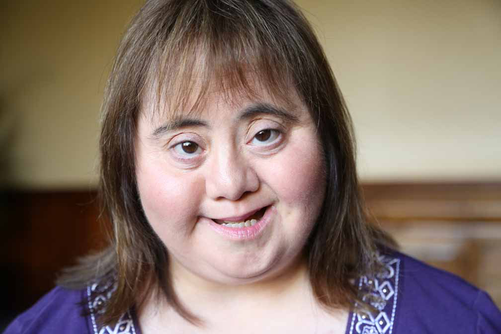 Woman with down syndrome in a purple dress smiling at camera