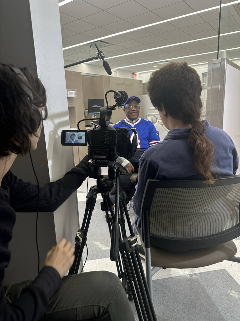 Man in blue shirt and baseball cap, on film set being interviewed,