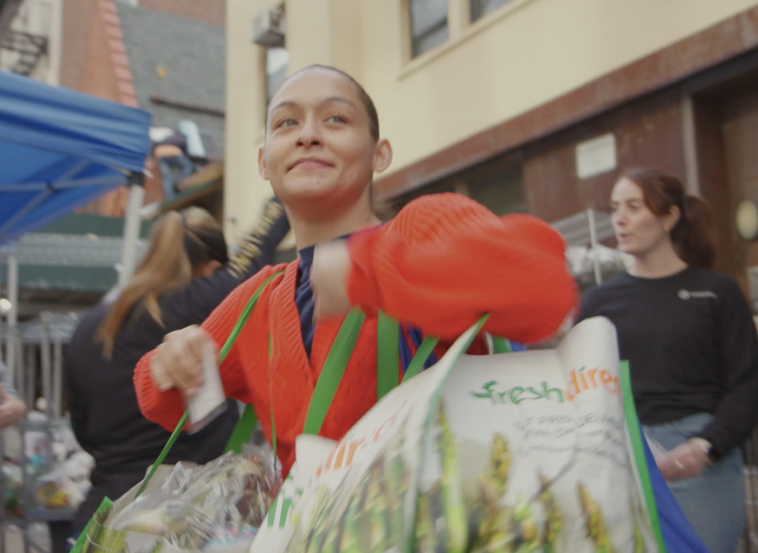 Woman wearing a bright orange sweater carrying a shopping bag over her shoulder.