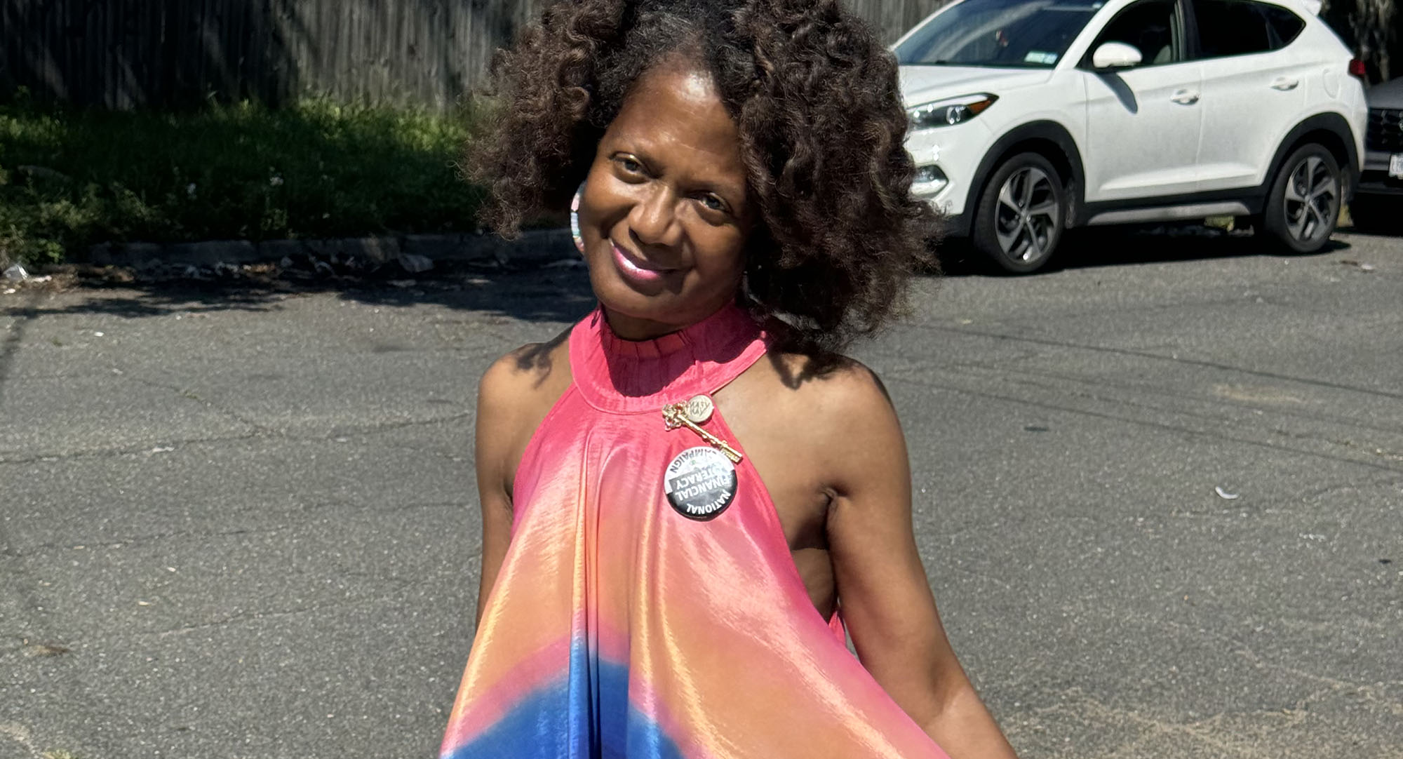 Woman with brown curly hair in a brightly colored summer dress. She is smiling.