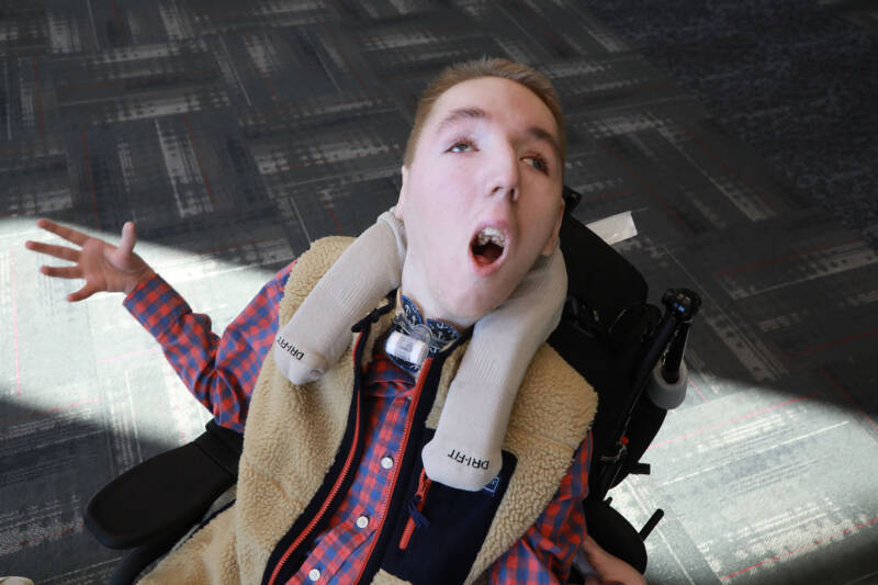 Young man with his arms outstretched looking into the camera. There is a patch of sunlight on the floor behind him.