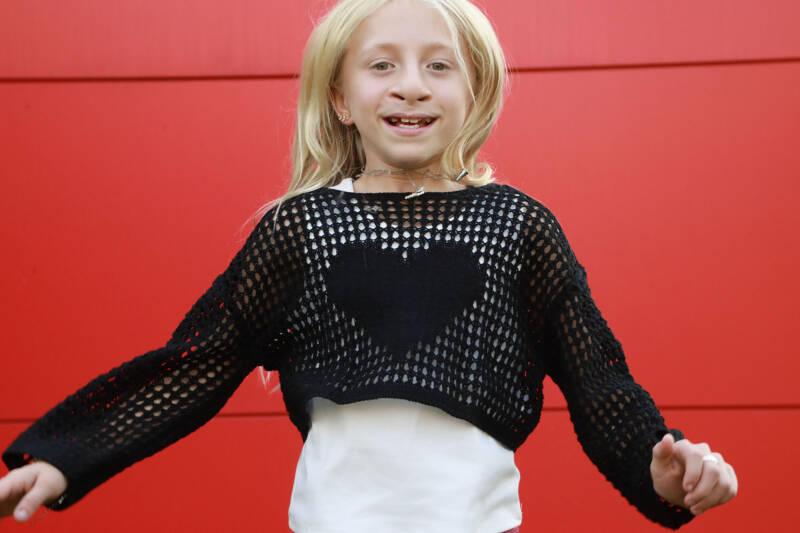 young girl with blond hair jumping against red wall