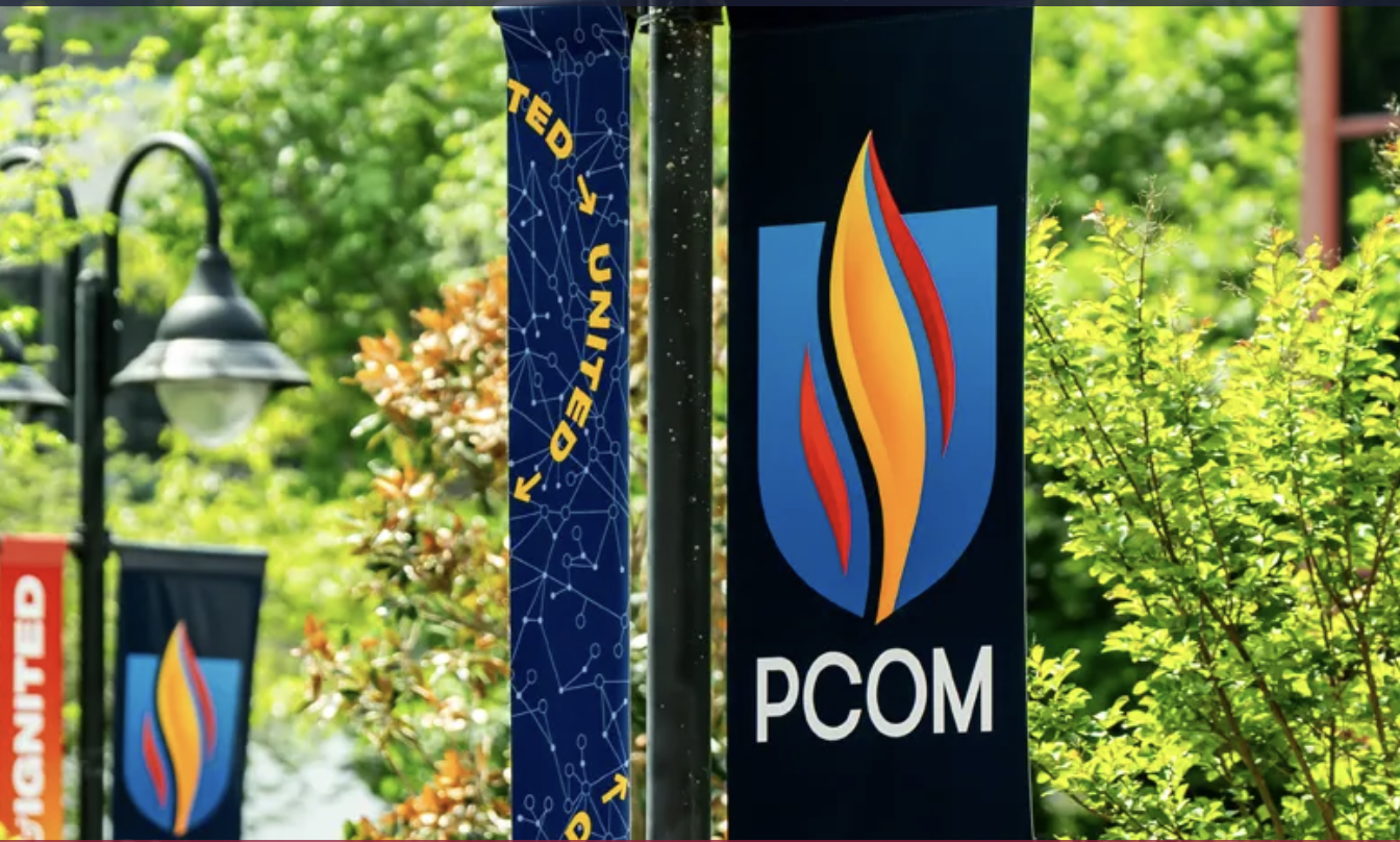 Outdoor shot of street flag with PCOM logo against a backdrop of trees.