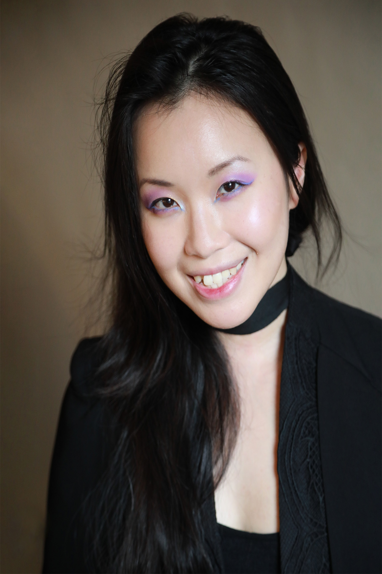 Woman with pale skin and dark hair wearing a black blazer is smiling into the camera
