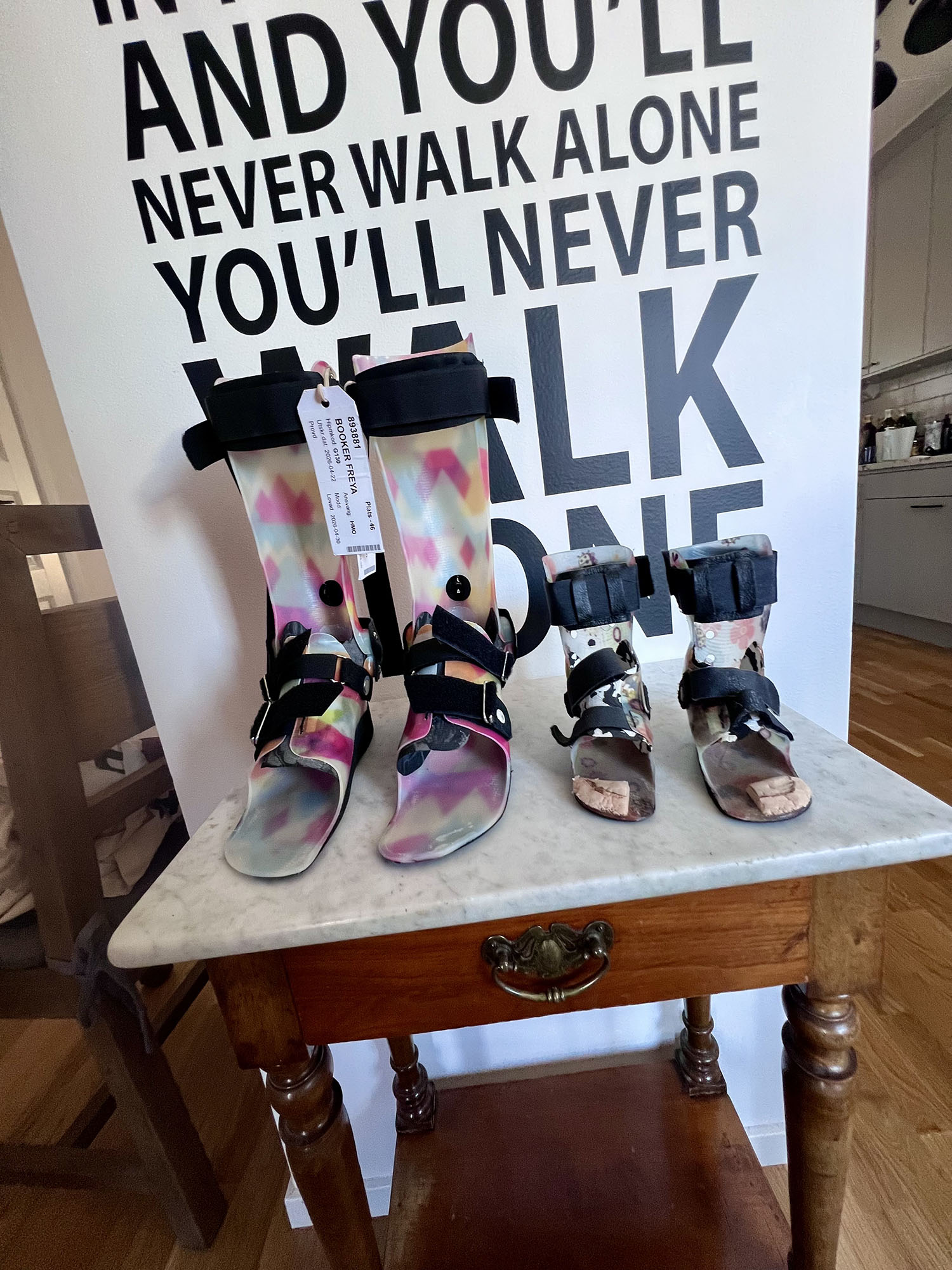 2 pairs of support shoes against a background that reads "You'll never walk alone"