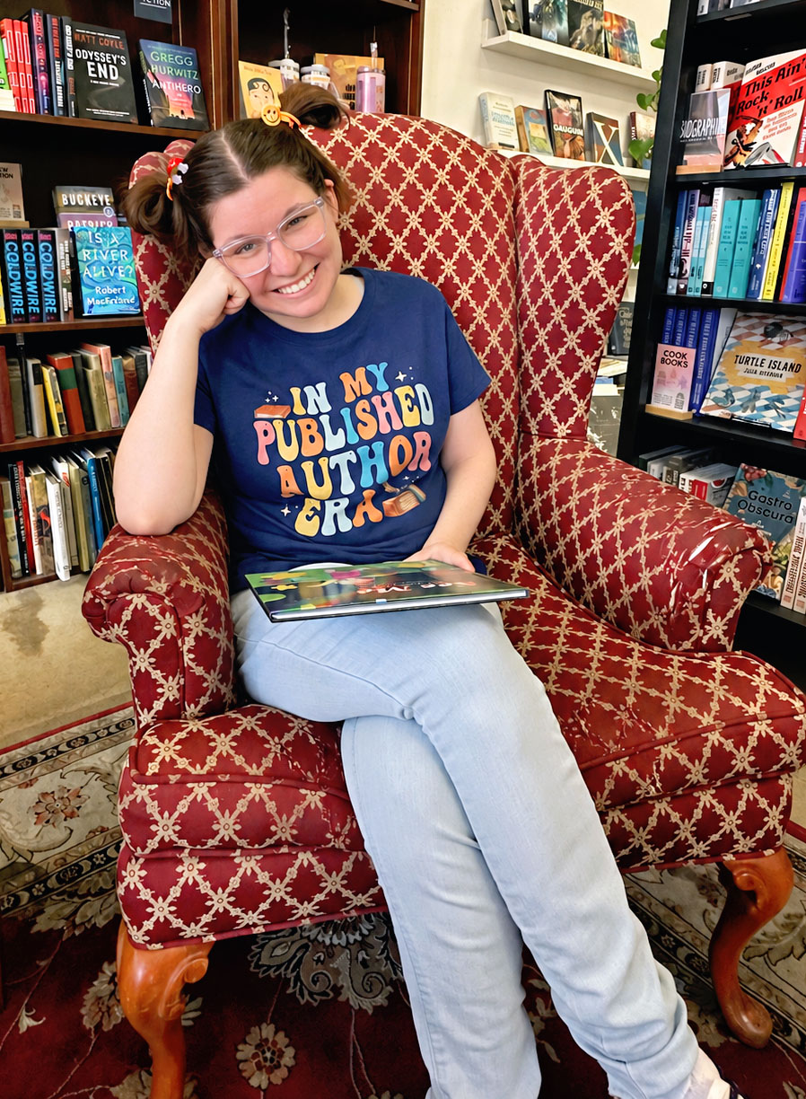 A young lady sitting in a chair holdingh a book and smiling