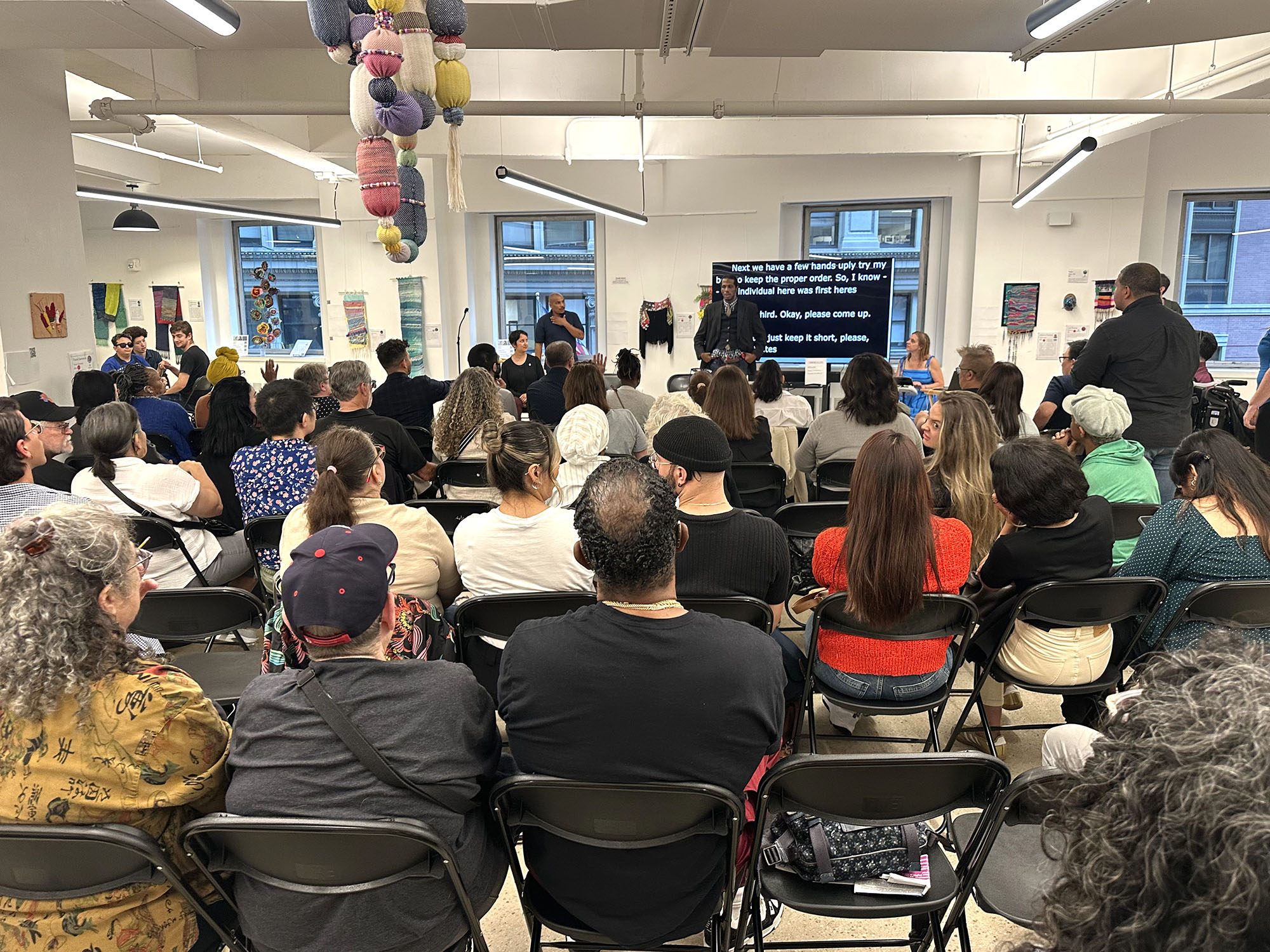 large group of people facing a speaker and ASL sign language interpreter at the gallery space